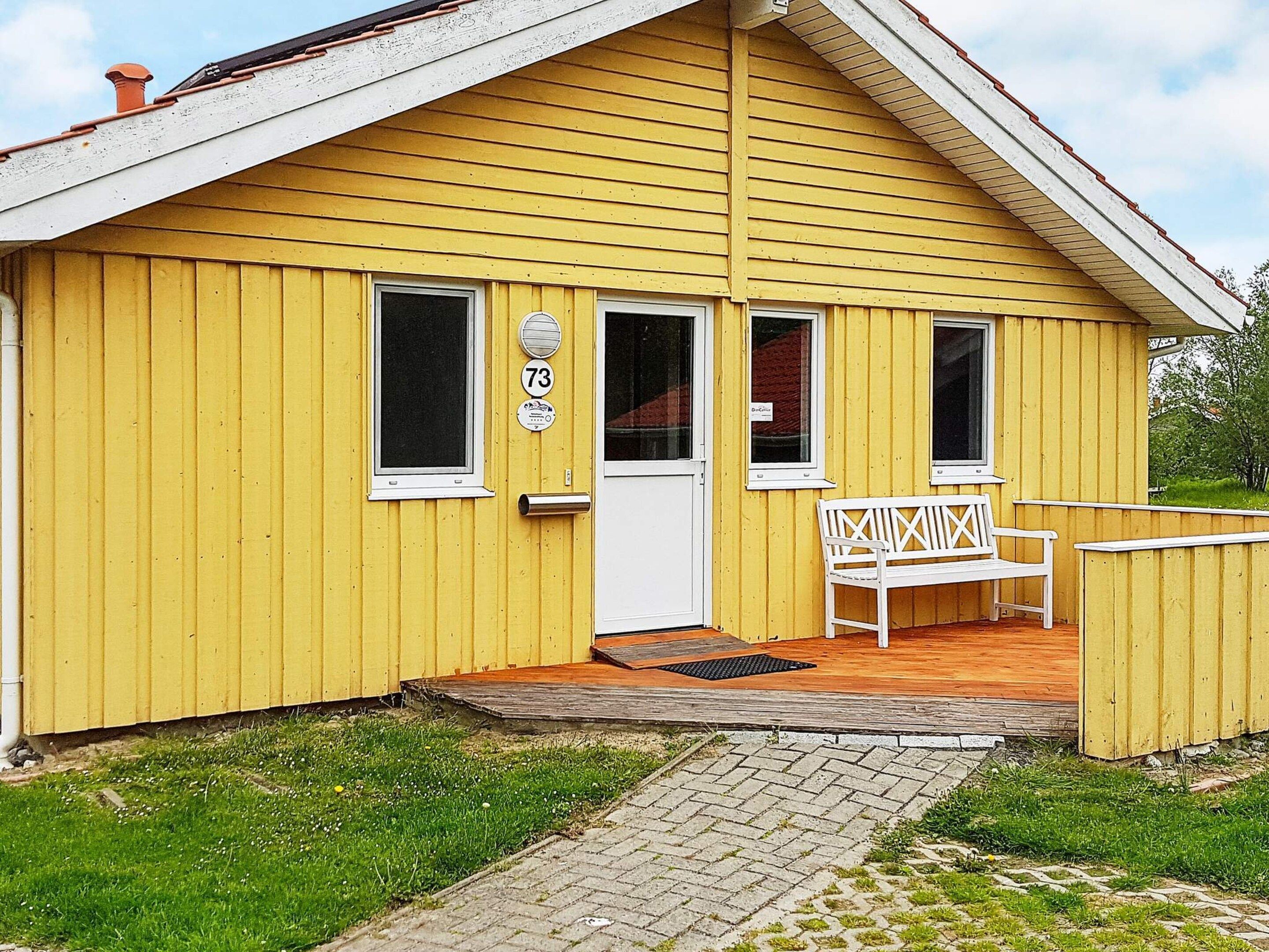 A yellow building with a white door, two windows, and a bench outside.