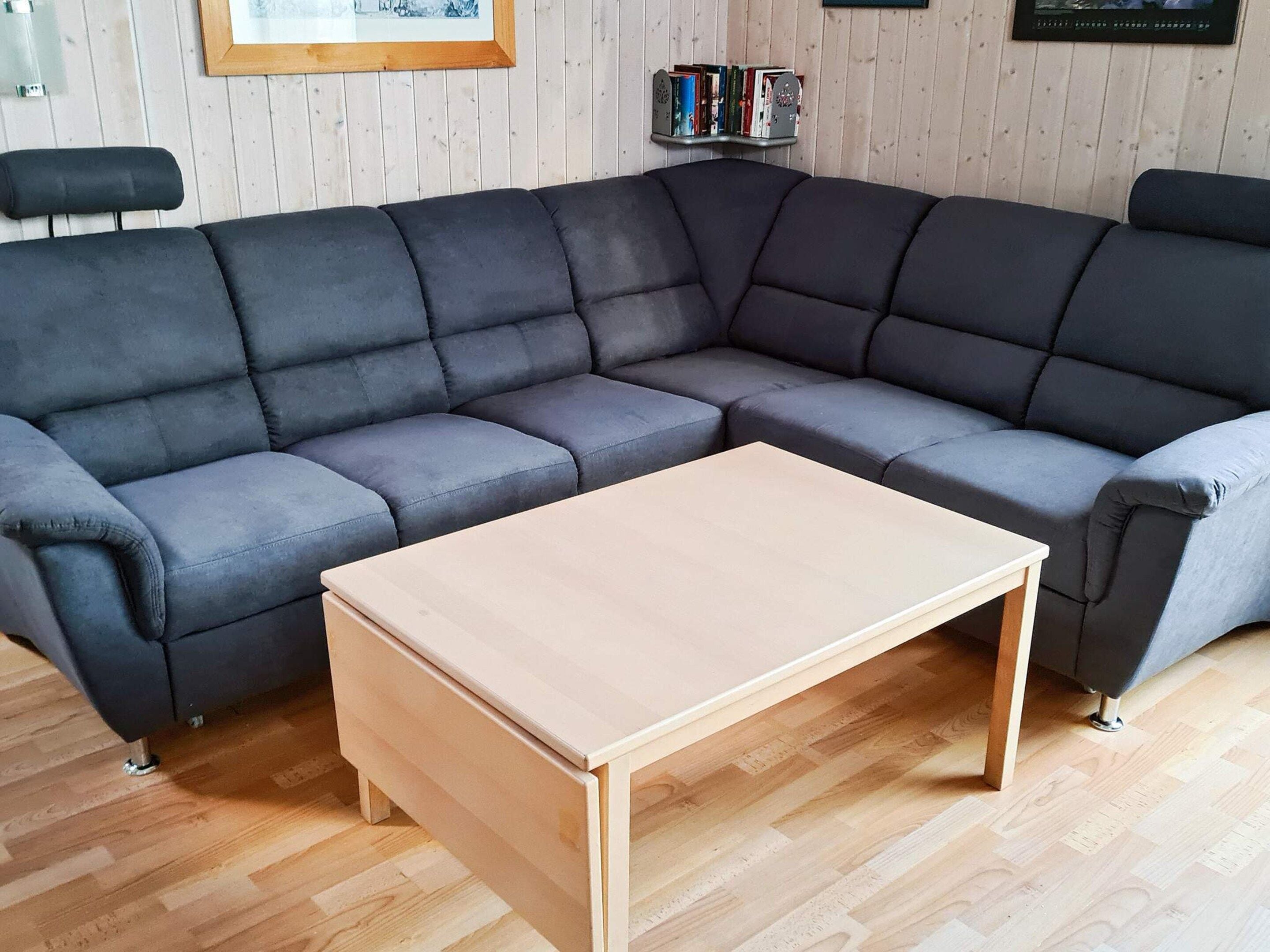 A modern living room with a sectional sofa, a wooden coffee table, and a bookshelf against a wooden wall.