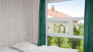 A bedroom with a bed, a window, and a view of a house and greenery outside. - Holiday Home in Otterndorf (Otterndorf)