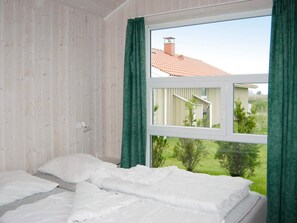 A bedroom with a bed, a window, and a view of a house and greenery outside. - Holiday Home in Otterndorf (Otterndorf)