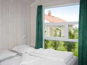 A bedroom with a bed, a window, and a view of a house and greenery outside. - Holiday Home in Otterndorf (Otterndorf)