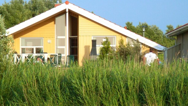 A yellow building with a large window and a door, surrounded by tall grass. - Holiday Home in Otterndorf (Otterndorf)