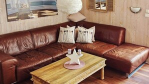 A brown leather sofa with decorative pillows, a wooden coffee table with a white star-shaped centerpiece, and a painting of a beach scene on the wall. - Holiday Home in Otterndorf (Otterndorf)