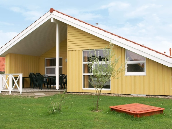 Ein gelbes Gebäude mit einem weißen Dach, einer überdachten Terrasse mit Stühlen und einem kleinen Baum.