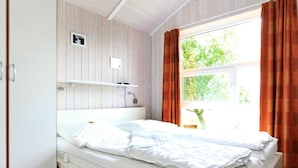 A single-bed room with a wooden wall, a window with curtains, and a bedside table. - Holiday Home in Otterndorf (Otterndorf)