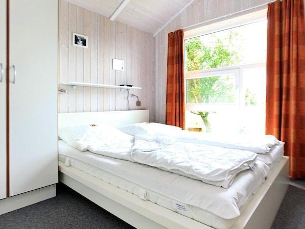 A single-bed room with a wooden wall, a window with curtains, and a bedside table. - Holiday Home in Otterndorf (Otterndorf)