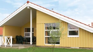 A yellow building with a pitched roof, a covered patio area with chairs, and a small tree. - Holiday Home in Otterndorf (Otterndorf)