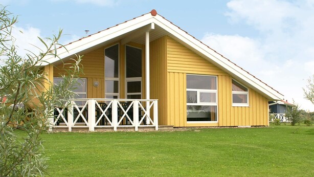 A yellow building with a white porch and a fenced area. - Holiday Home in Otterndorf (Otterndorf)