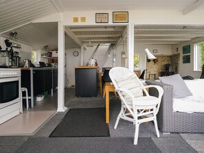 A compact kitchen with a stove, sink, and coffee maker, a dining area with a chair and table, and a cozy seating area with a sofa and cushions. - Lovely Holiday Home in AsnÃ¦s near Sea (Asnaes)