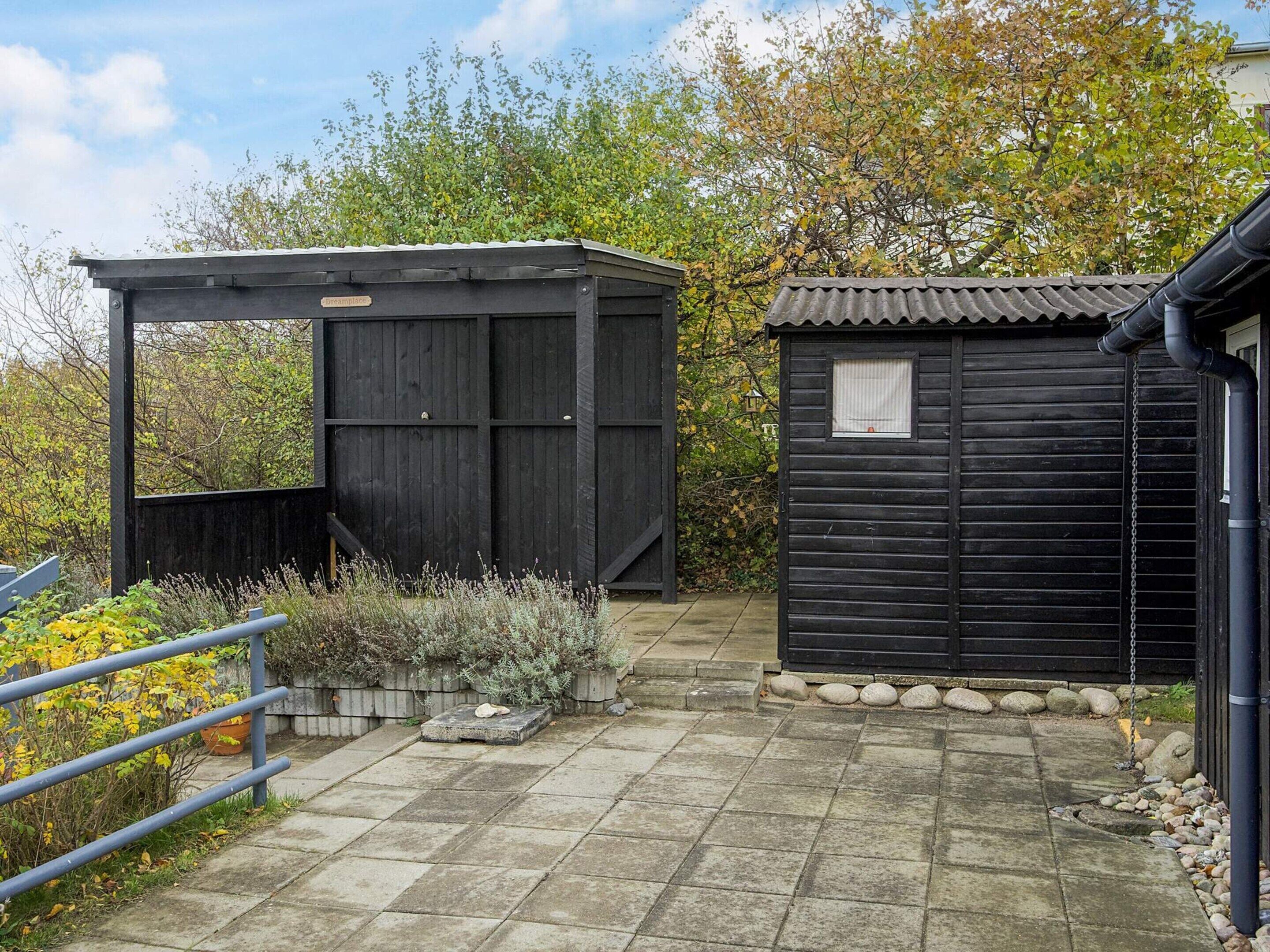 Un abri en bois avec un toit ondulé, un chemin pavé de pierres et une rambarde en métal.