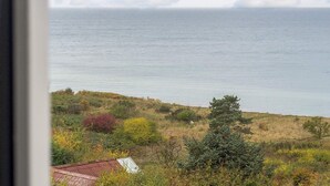 A coastal landscape with a view of the sea, a house with a red roof, and surrounding vegetation. - Lovely Holiday Home in AsnÃ¦s near Sea (Asnaes)