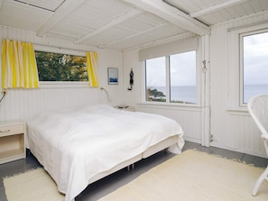 A bedroom with a bed, a nightstand, a chair, and a window with a view of the sea.