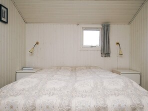 Un dormitorio con una cama, dos mesitas de noche, un ventanal y una cortina.