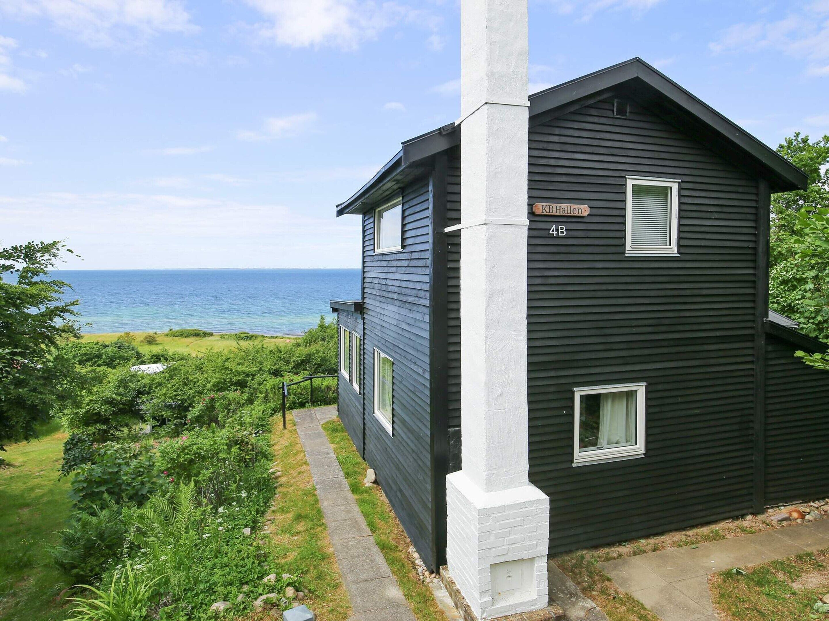A two-story house with a black exterior and white trim, labeled 'KBHallen 4B,' located near a body of water.