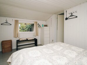 A bedroom with a bed, a bench, a hanging clothes rack, and a window with curtains. - Lovely Holiday Home in AsnÃ¦s near Sea (Asnaes)