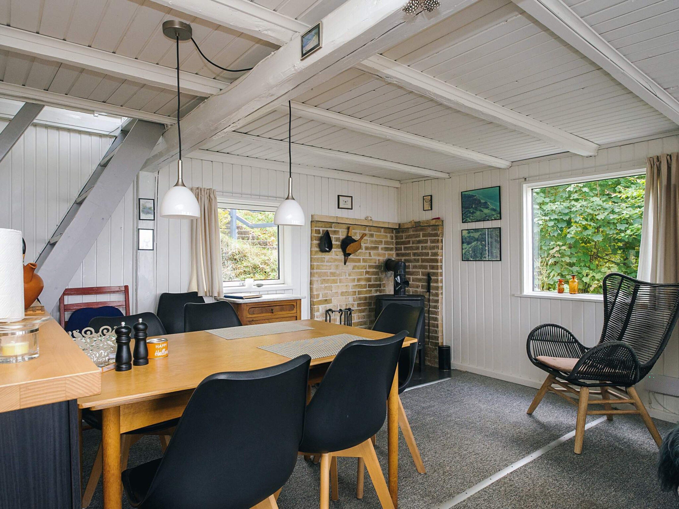 A dining area with a wooden table, black chairs, pendant lights, a brick wall, and a window with greenery outside.