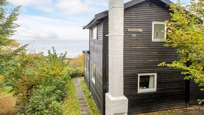 A two-story house with a dark exterior, a visible chimney, and a small window. - Lovely Holiday Home in AsnÃ¦s near Sea (Asnaes)