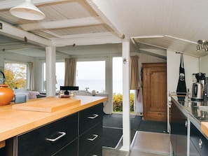 A kitchen with a wooden countertop, black cabinets, a coffee maker, and a view of the sea.
