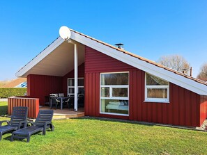 A red house with a sloped roof, a satellite dish, and a patio with chairs and a table. - Holiday Home in Otterndorf (Otterndorf)