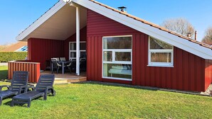 A red single-story house with a sloped roof, a satellite dish, and a patio with outdoor furniture. - Holiday Home in Otterndorf (Otterndorf)