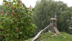 A playground with a slide and a wooden structure, surrounded by green grass and trees. - Holiday Home in Otterndorf (Otterndorf)