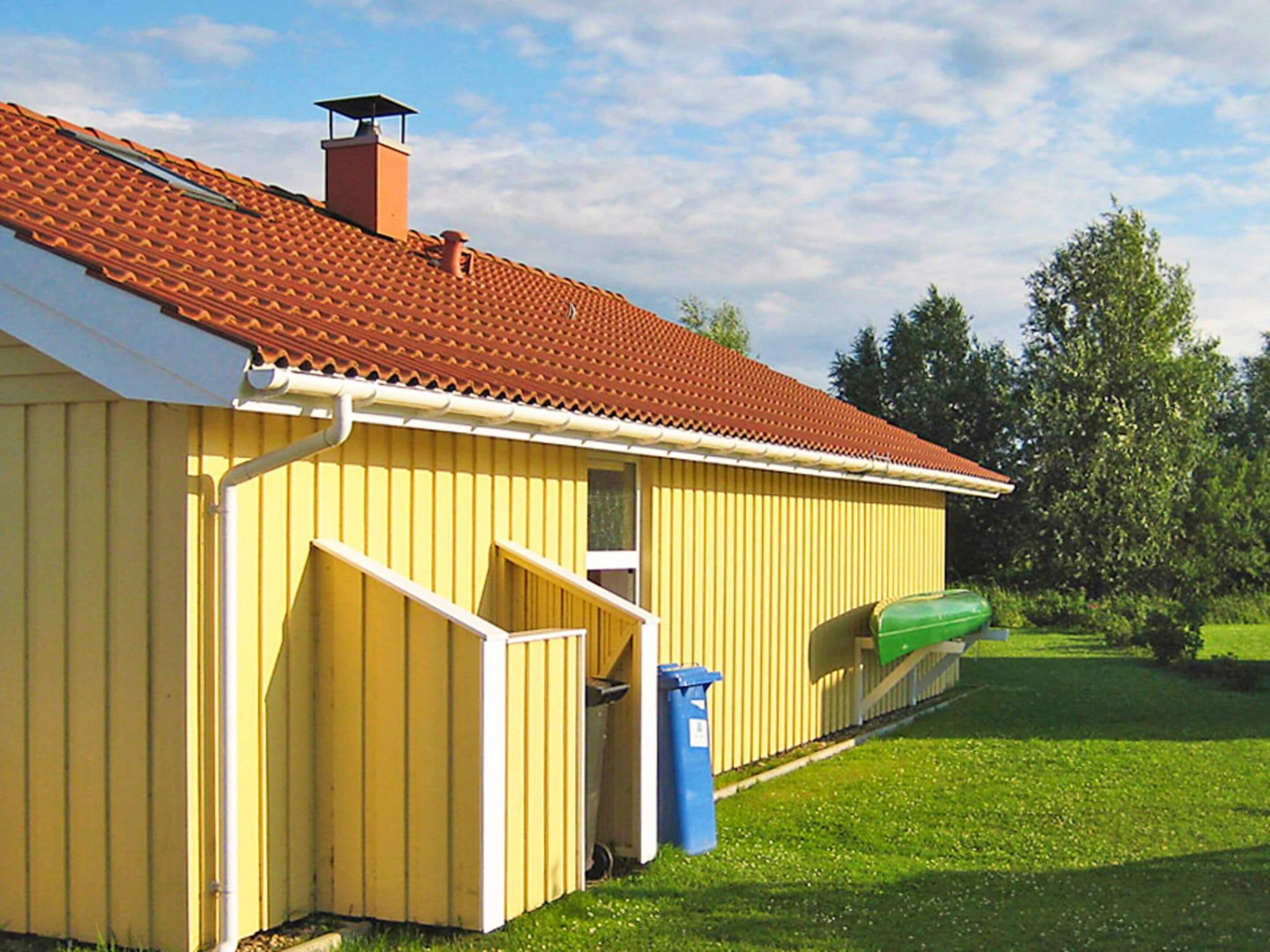 A yellow building with a red-tiled roof, a chimney, and a green kayak on the grass.