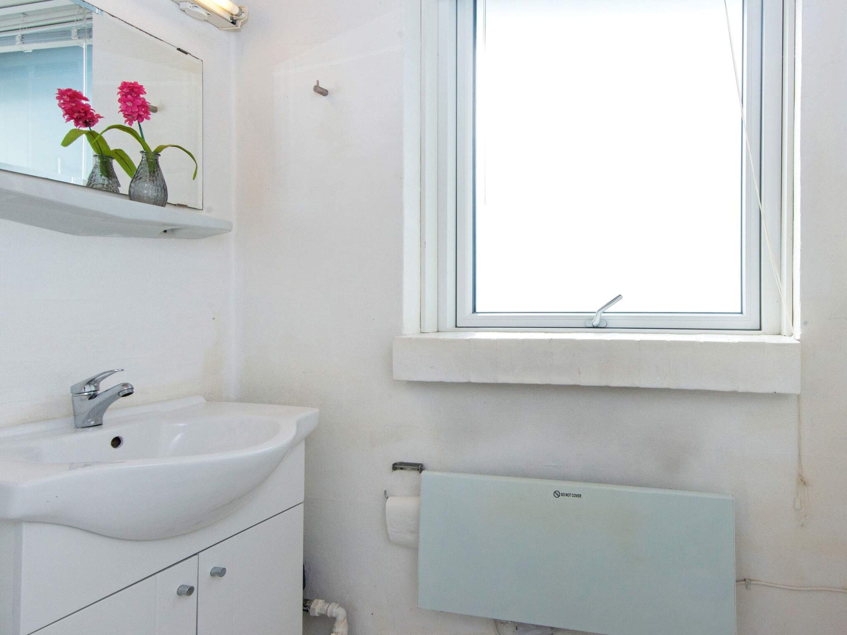 A bathroom with a white sink, mirror, and window.