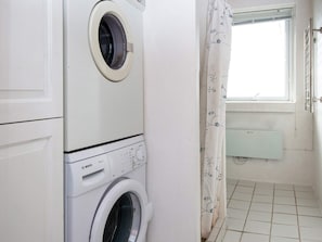 A laundry room with stacked washing machines, a window with a view, and a radiator. - 8 Person Holiday Home in Harboore (Harboore)
