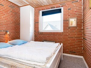 A bedroom with a brick wall, a window with a blind, a bed with pillows, and a wardrobe. - 8 Person Holiday Home in Harboore (Harboore)