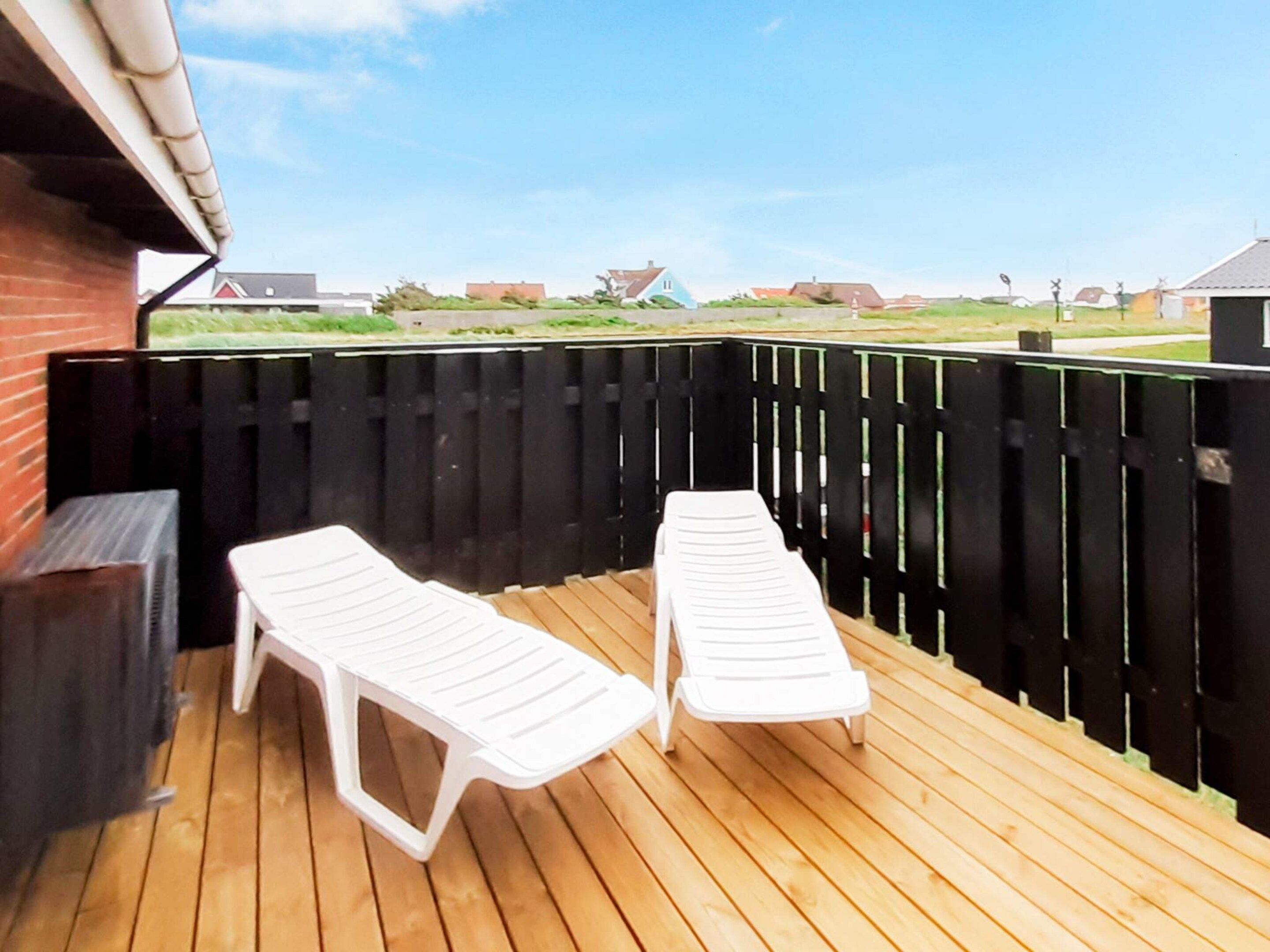 Una terraza de madera con dos sillones blancos, un muro de ladrillo y una valla negra.
