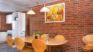 Un coin repas avec un mur en briques, un réfrigérateur blanc, une cuisinière et un tableau représentant des fleurs.