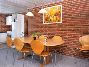 A dining area with a brick wall, a white refrigerator, a stove, and a painting of flowers. - 8 Person Holiday Home in Harboore (Harboore)