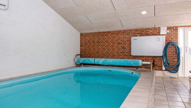 Une piscine avec un sol carrelé, un mur en briques et un tableau blanc fixé au mur.