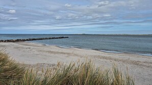 Une plage dotée d’une digue rocheuse, d’un rivage sablonneux et de dunes herbeuses.