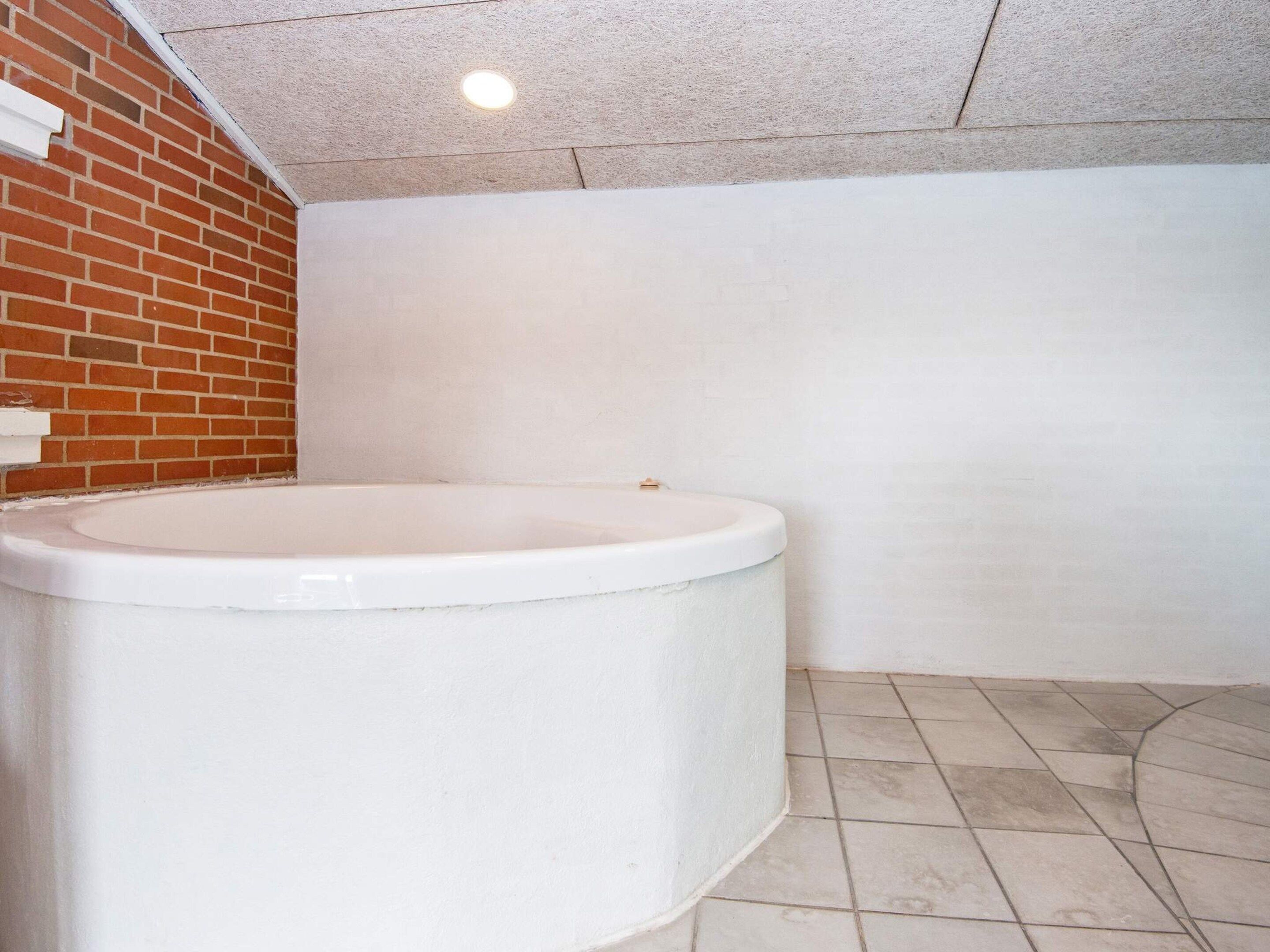 A bathroom with a white bathtub, a tiled floor, and a brick wall.