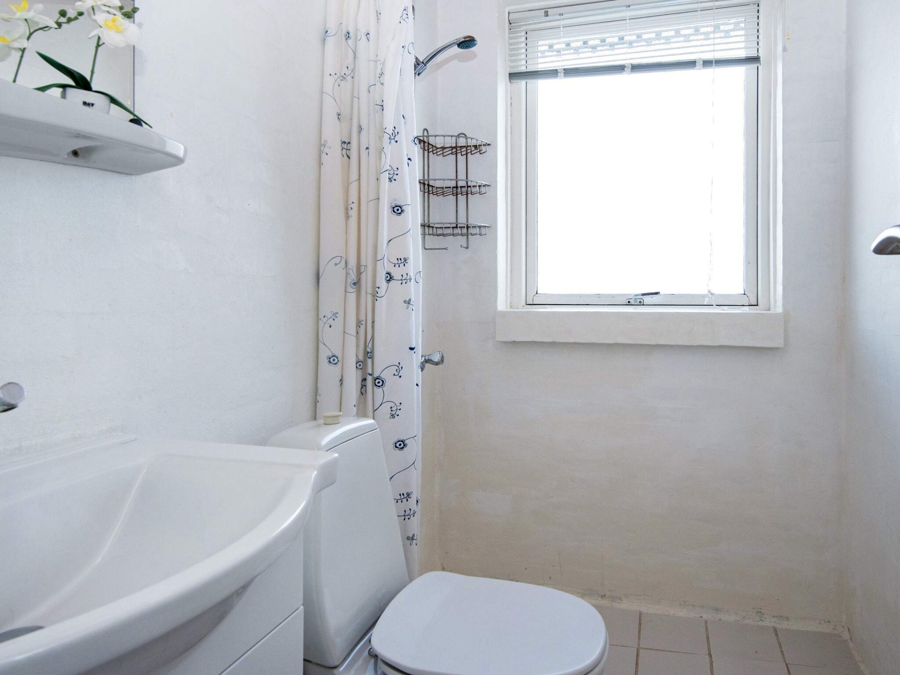 Et badeværelse med toilet, brusebad og et vindue.
