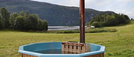 A hot tub on a wooden deck with a view of a lake and mountains in the background.