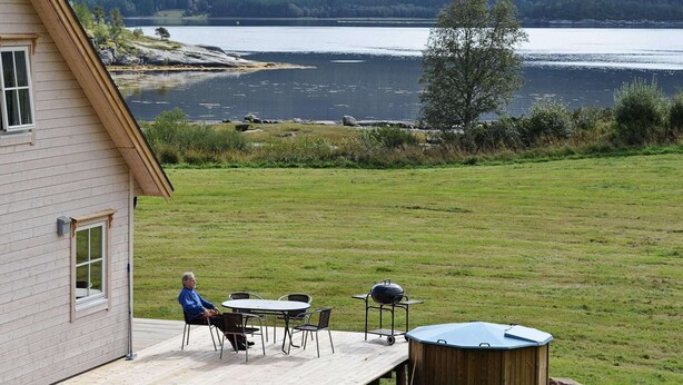 A house with a deck overlooking a lake, a barbecue setup, and a wooden shed. - Holiday Home in FÃ¸llenslev (Nærøysund)