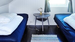 A small, cozy room with two single beds, a small table with a lamp, a window with curtains, and a framed picture on the wall. - Holiday Home in FÃ¸llenslev (Nærøysund)