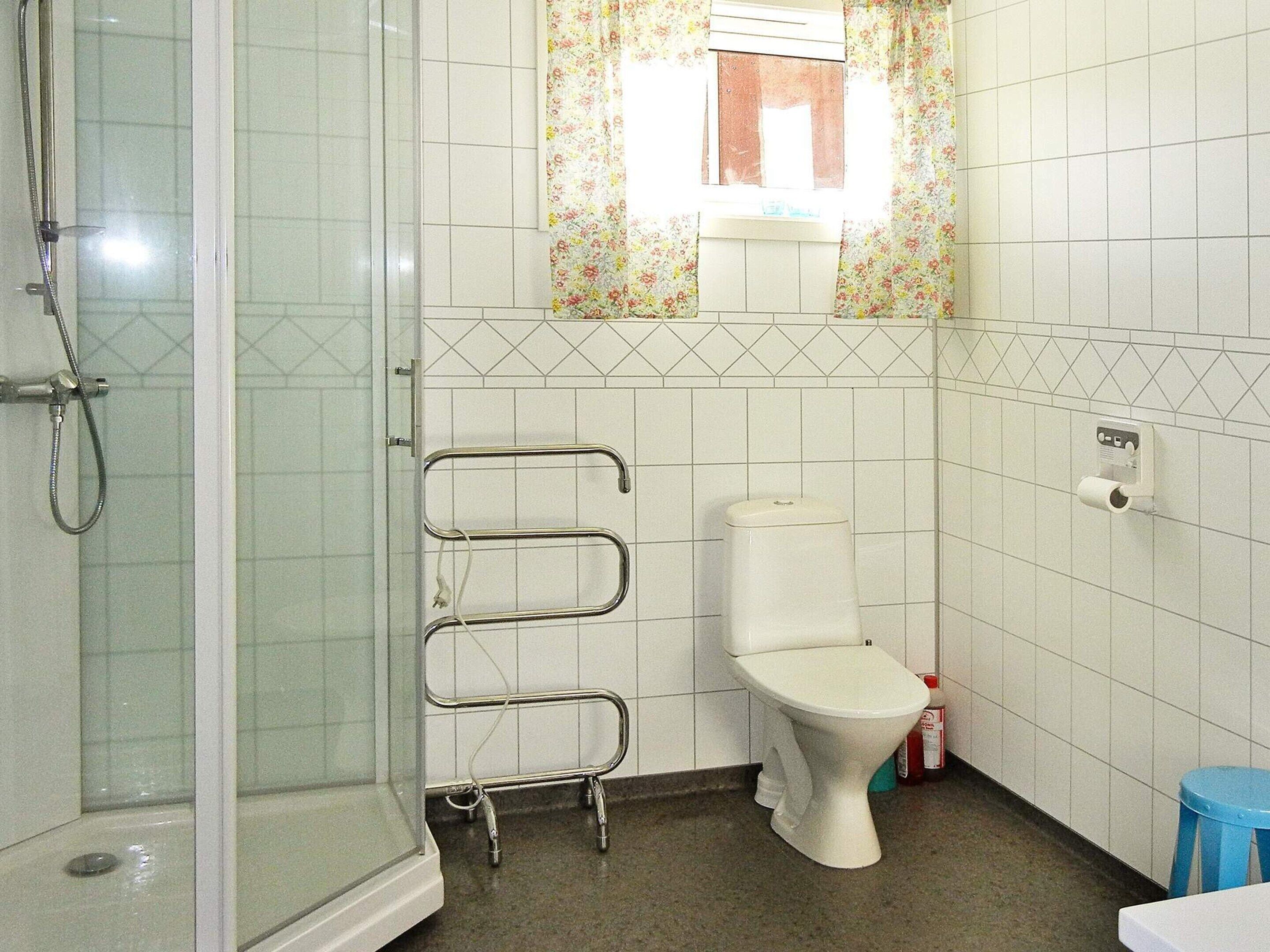 A bathroom with a shower, toilet, and a small stool.
