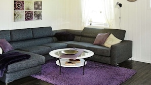 A living room with a sectional sofa, a round coffee table, and a purple rug. - Holiday Home in FÃ¸llenslev (Nærøysund)