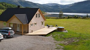 A two-story house with a sloped roof, a covered porch, and a view of a lake and mountains. - Holiday Home in FÃ¸llenslev (Nærøysund)