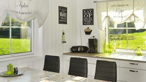 A dining area with a table covered in a floral tablecloth, chairs, a coffee maker, and decorative items on the windowsill. - Holiday Home in FÃ¸llenslev (Nærøysund)