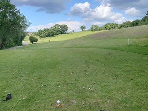 A golf course with a clear path, trees, and a distant building.