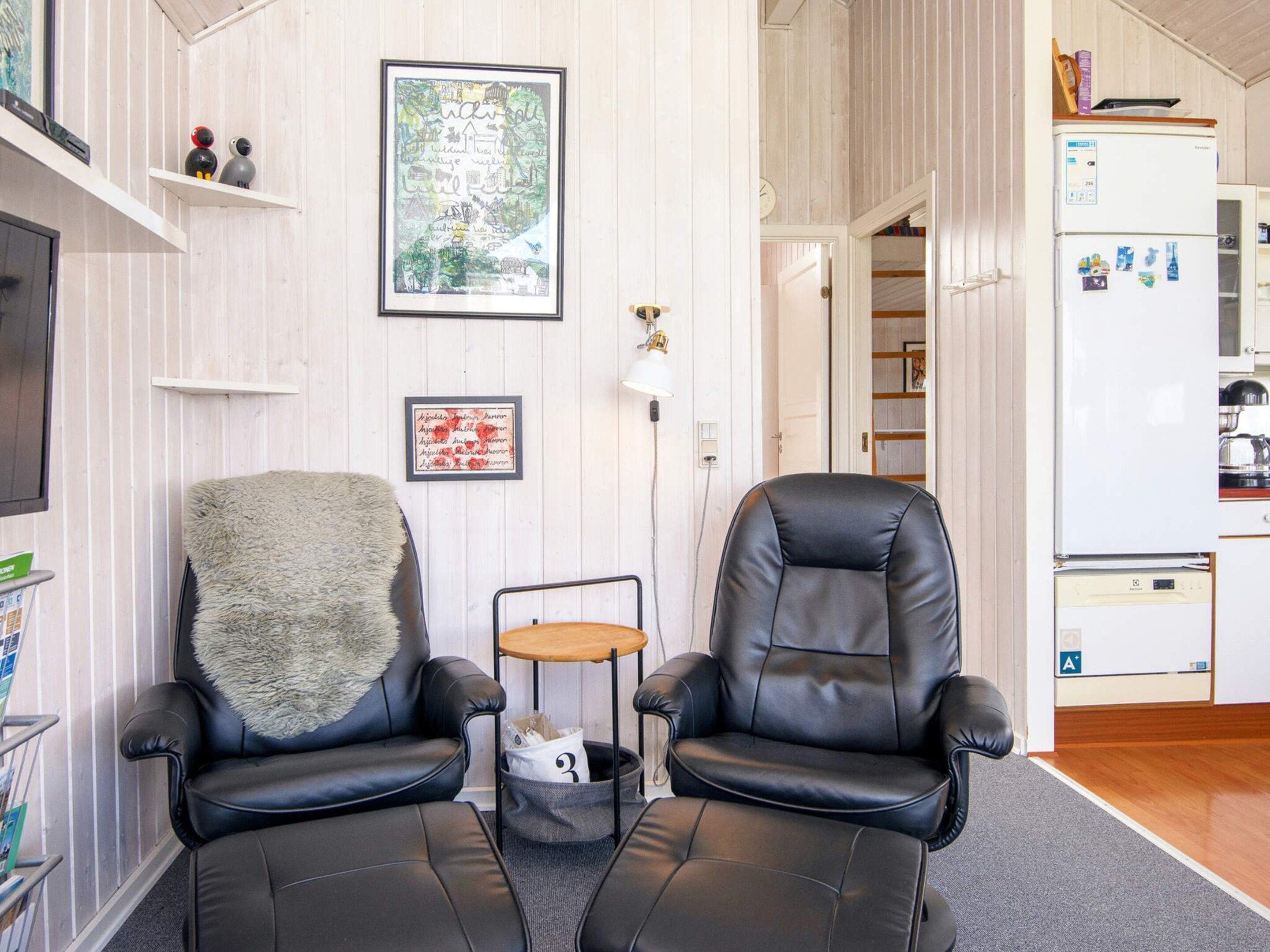 A living room with two black leather chairs, a small table, a fluffy throw, and a framed map on the wall.
