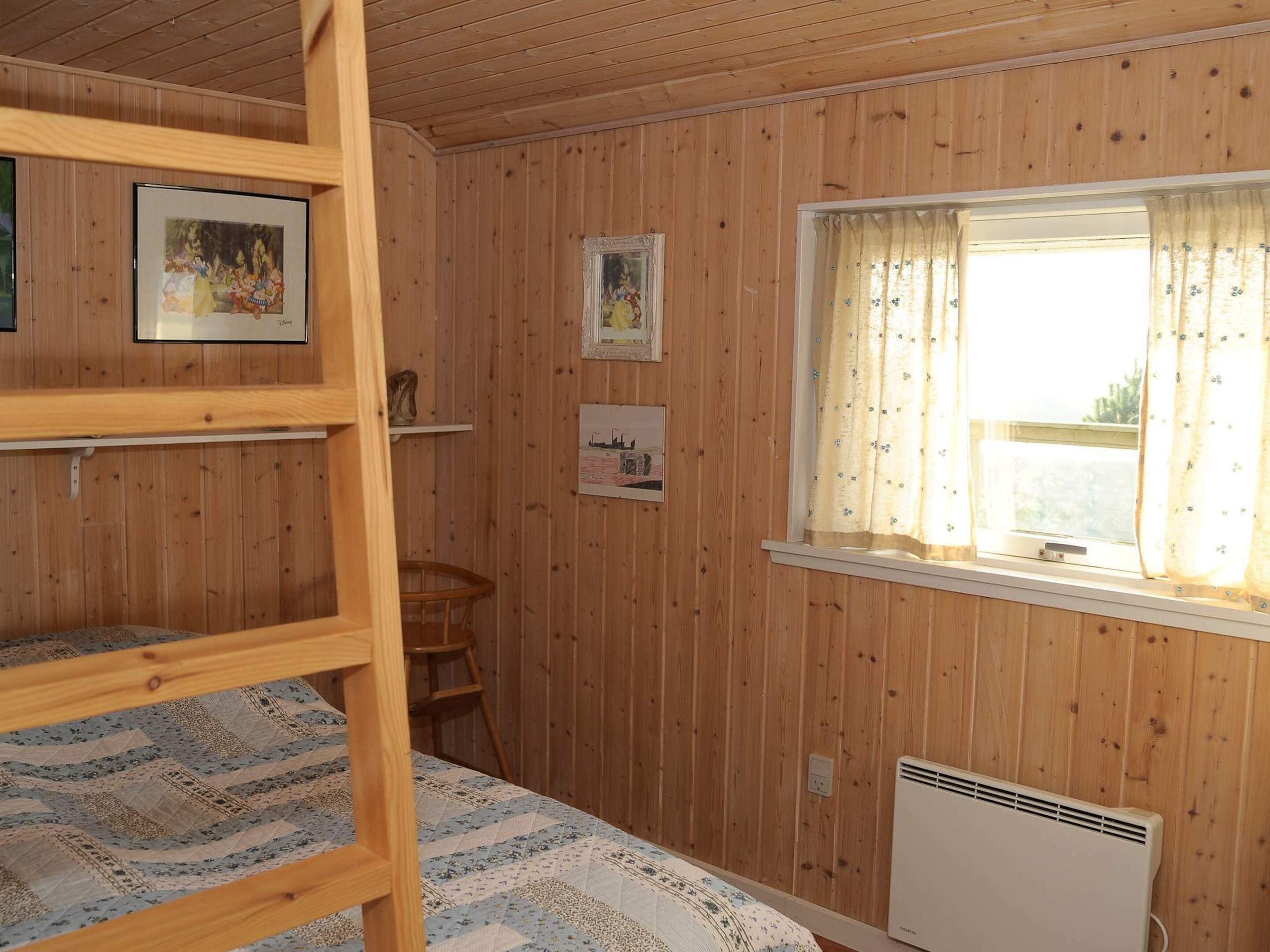 Una habitación con paneles de madera, literas, una ventana con cortinas e imágenes colgadas en la pared.