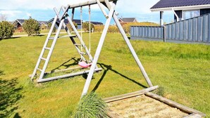A wooden swing set in a grassy yard with a house in the background. - Lovely Holiday Home in Lemvig near Sea (Lemvig)