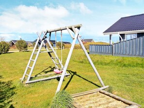 Een houten schommel in een gazon met een huis op de achtergrond.