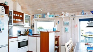 A compact kitchen with white cabinets, a stove, and a coffee maker. There is a window above the sink, and various kitchen items are displayed on the shelves. - Lovely Holiday Home in Lemvig near Sea (Lemvig)