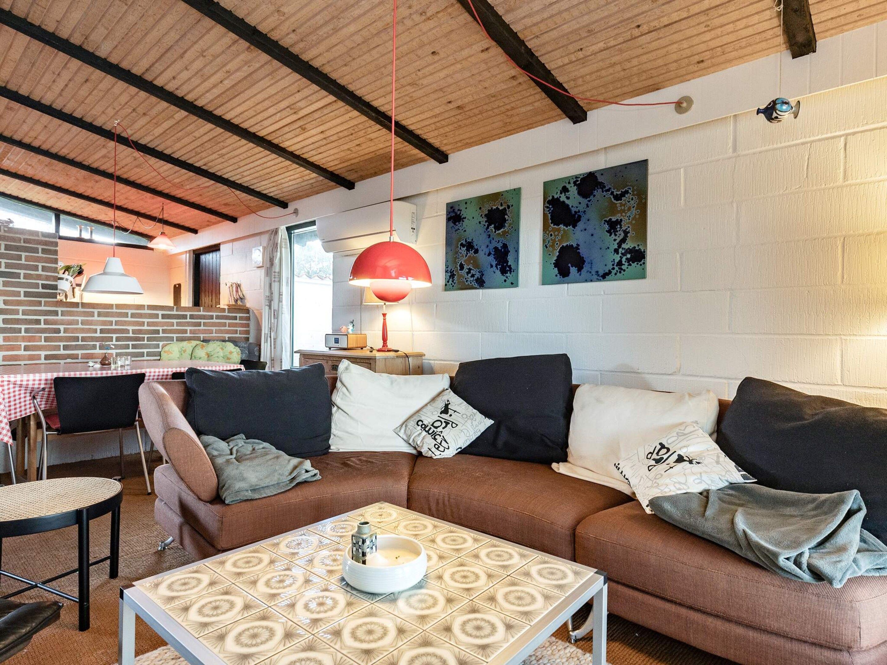 Un salón acogedor con un sofá marrón, una mesa de centro estampada y una lámpara colgante roja.